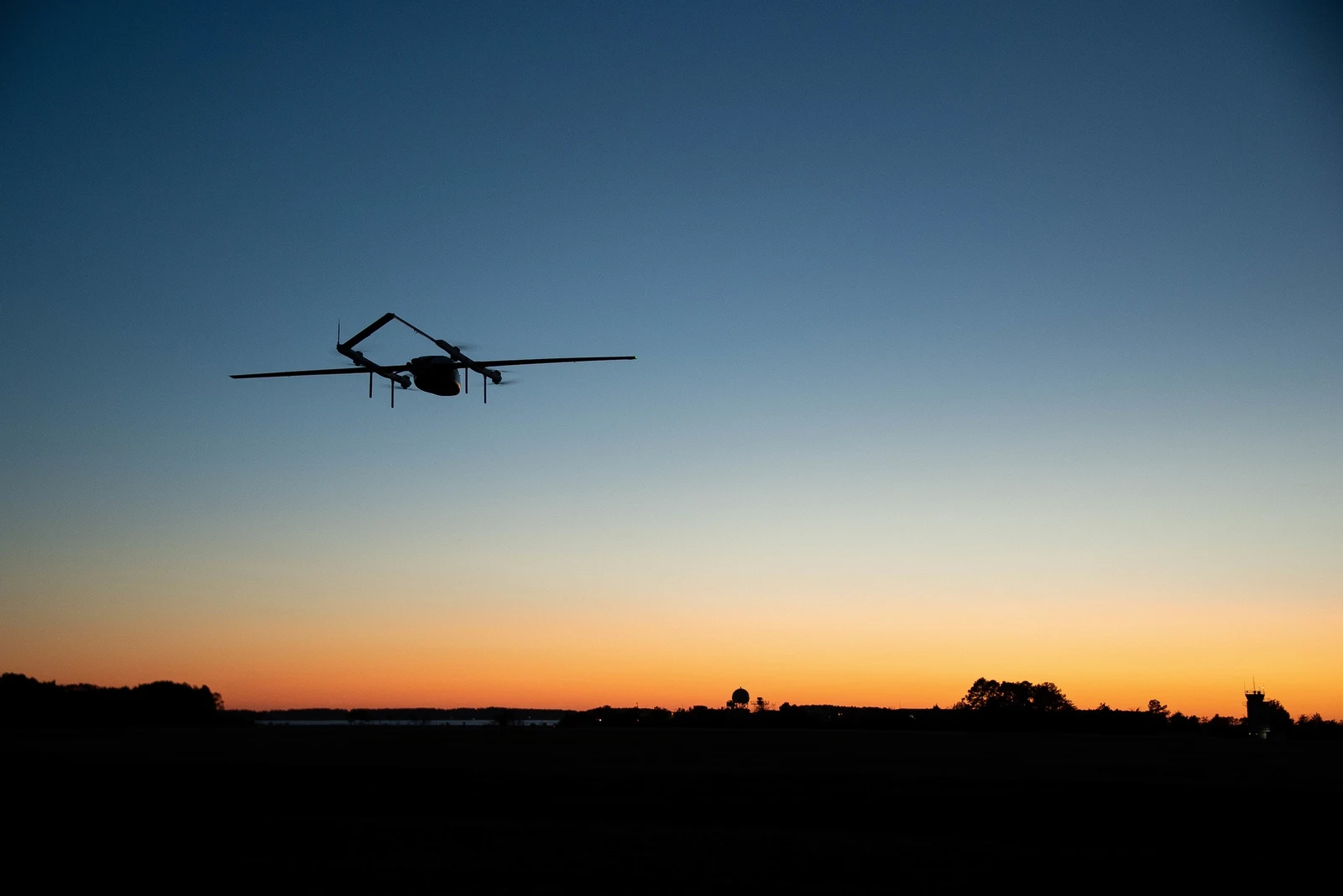 A Group 3 uncrewed aircraft flies over a test range at dusk.